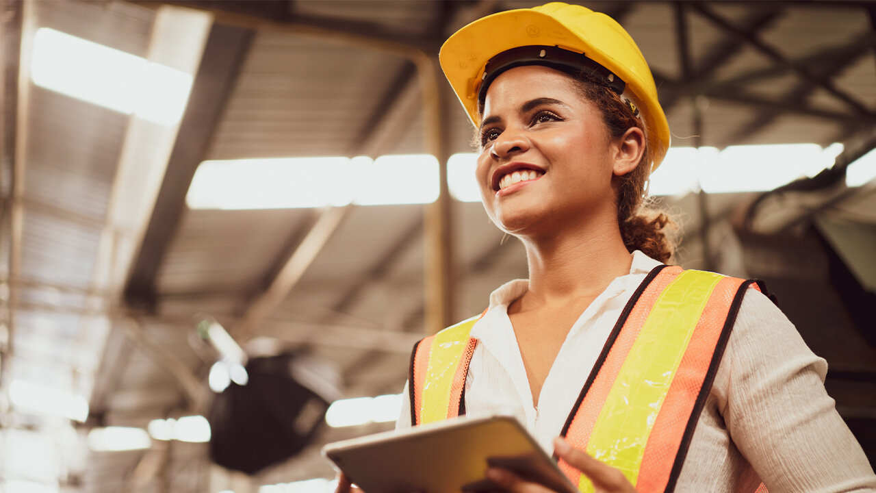Jeune femme portant un casque et un gilet de chantier utilisant une tablette